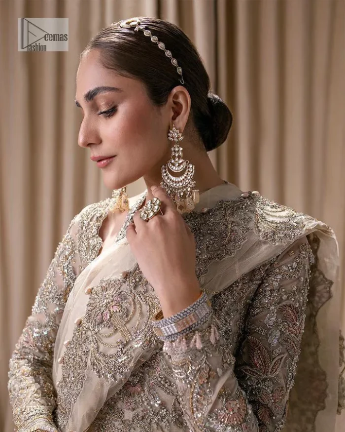 Make a statement with a light fawn article on your nikah day! DeemasFashion presents the light fawn heavy maxi which is embellished with silver embroidery using dabka, tilla, kora, Zardozi, Swarovski, Mukesh, sequin and Kundan. The strap neckline adds a little romanticness to the dress. Further, the floral patterns on full sleeves make this masterpiece modern and unique. It is paired with a  lehenga, embellished with a delicate border. It is styled with a dupatta; its surface is sprayed with sequin and the dupatta is enveloped by a heavily embellished floral border.