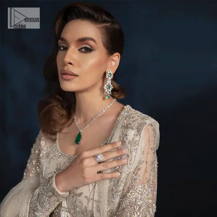 A sophisticated splash of off-white as your nikah outfit! With its round neckline and full sleeves, this outfit has a fine fusion look. Utilizing attractive silver embellishment work to enhance its intricate beauty. Tilla, dabka, kora, Kundan and the details of Zardozi beautifully embellish the elegant frock. It is paired with a flared lehenga to balance the overall look of this charming article. Finish this soft and bold look with a heavily bordered four-sided dupatta with a spray of sequins all over to make your Big day super aesthetic.