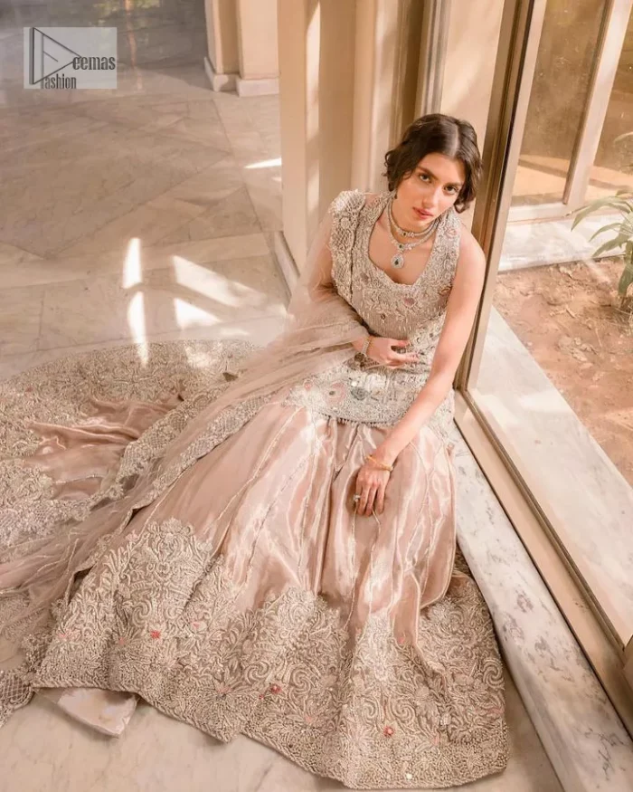 The beauty of idealism is captured with a touch of sparkle. This exclusive rose pink ensemble is beautifully translated on rose pink canvas, which makes this walima outfit stand out in the crowd. This fully embellished article comes with a short shirt lehenga style that gives it a bold look. The round neckline makes this masterpiece a unique cut. The short shirt is adorned with a silver embroidery which involves tilla, dabka, kora, Kundan and the real magic of Zardozi. Further, the sleeveless style of the following short shirt adds charm to the lehenga with heavy border embellishments on it. Carrying out its final contemporary look with a net scalloped dupatta framed with four-sided embellished borders and cross lines all over.