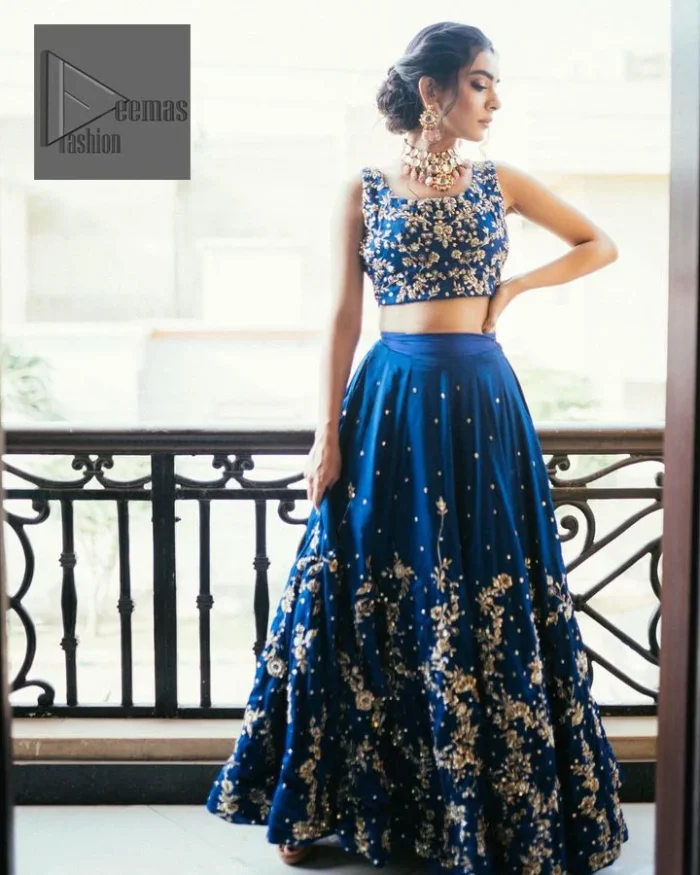  Highlight your entire look and add a touch of sophistication with delicate details. This Party outfit from DeemasFashion is a stunning masterpiece that captures everyone's heart with its charm and elegance upon very first glance. The Royal blue blouse is adorned with Golden embroidery, making it a head-turning masterpiece. Moreover, the square neckline is fully embellished with tilla, dabka, kora, Kundan, and pearls, lending it a magical appearance. The sleeveless style adds a touch of allure to this already captivating outfit. It is paired with an embroidered lehenga to enhance your day's look, and the article is completed with a dupatta featuring tiny floral motifs and sequins sprayed all over.